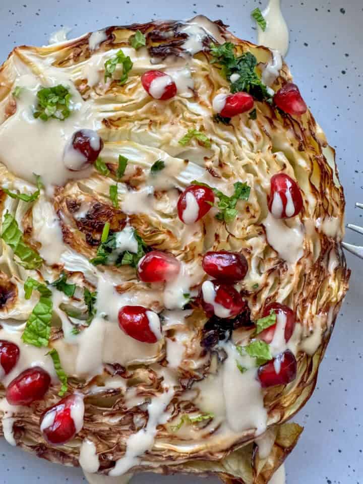 roasted cabbage on a plate drizzled with tahini and pomegranate seeds